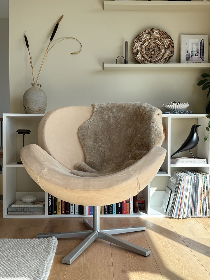 Beige chair with a brown cushion in a room with bookshelves and decorative items.
