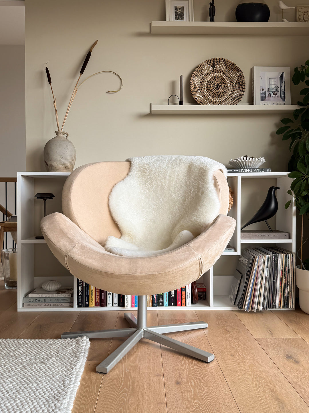 Beige armchair with white cushion in a room with bookshelves and decor items.