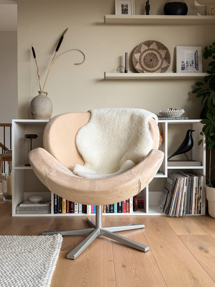 Beige armchair with white cushion in a room with bookshelves and decor items.