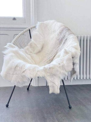 White reindeer hide rug over a modern chair in a minimalistic room.