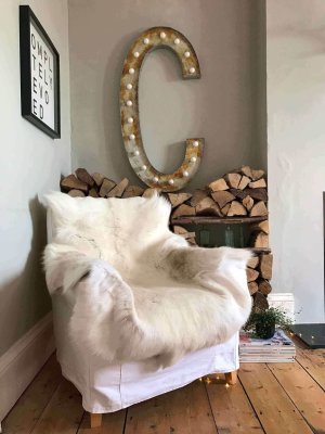 White fur-covered chair in a room with a large letter 'C' and stacked firewood.
